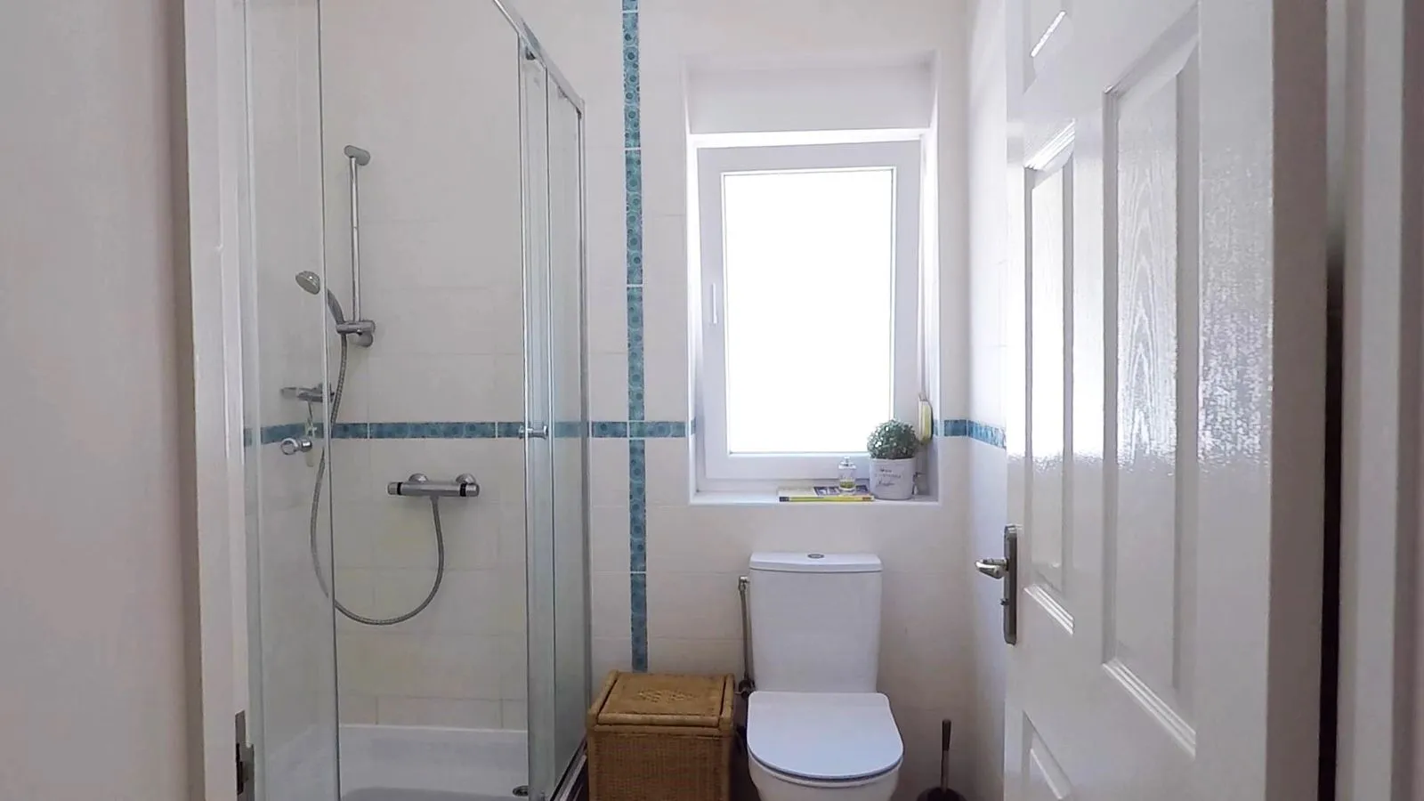 Bathroom featuring a glass shower enclosure, white toilet, window, and blue decorative tile accents on the walls.