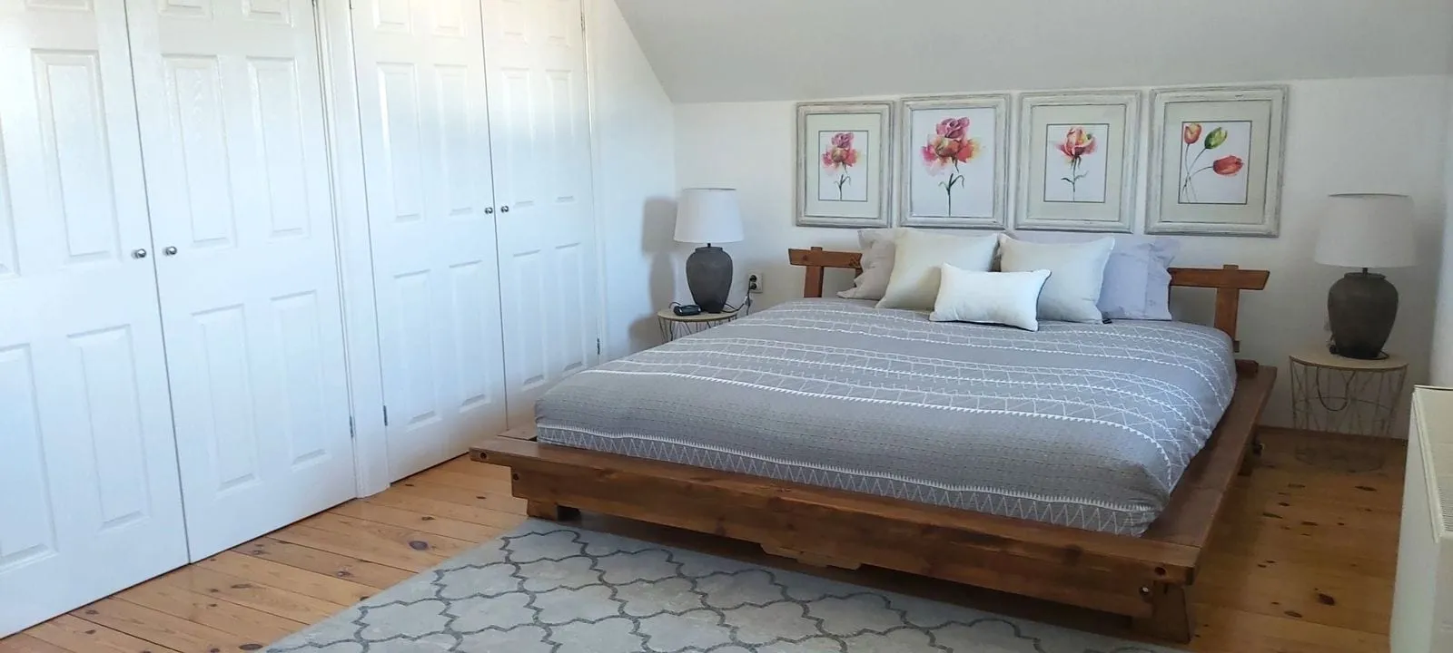 Bedroom featuring a wooden platform bed, gray bedding, white closet doors, and four floral art prints above the headboard.