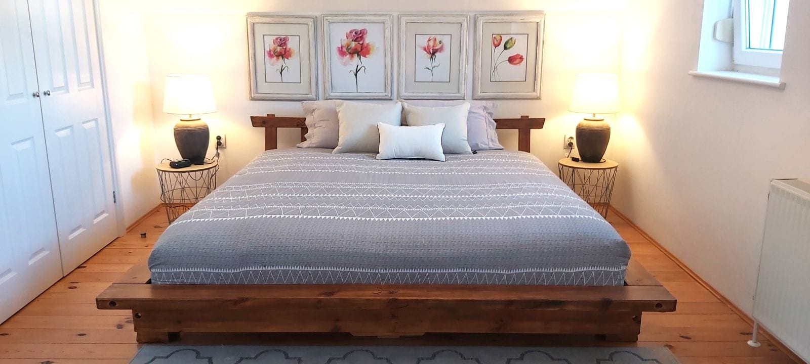Cozy bedroom with a wooden bed and paintings in a house, Krimovica, Montenegro. Bright interior with parquet flooring.