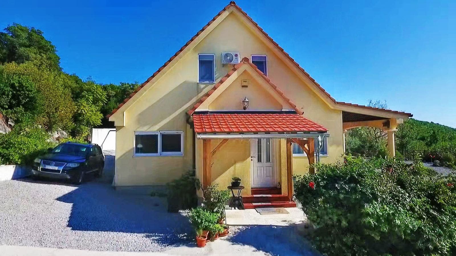 Two-story private house with a tiled roof and parking in the village of Krymovitsa, Montenegro, front view of the building.