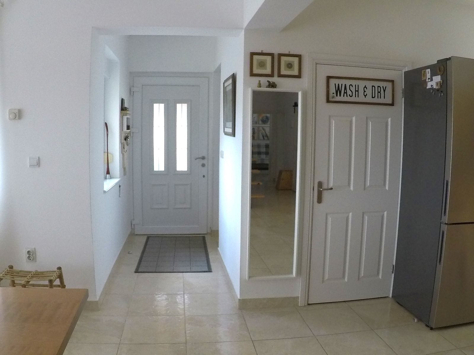 Bright hallway in the house, Krymovitsa, Montenegro: white front door, mirror, and laundry room door with a Wash & Dry sign.