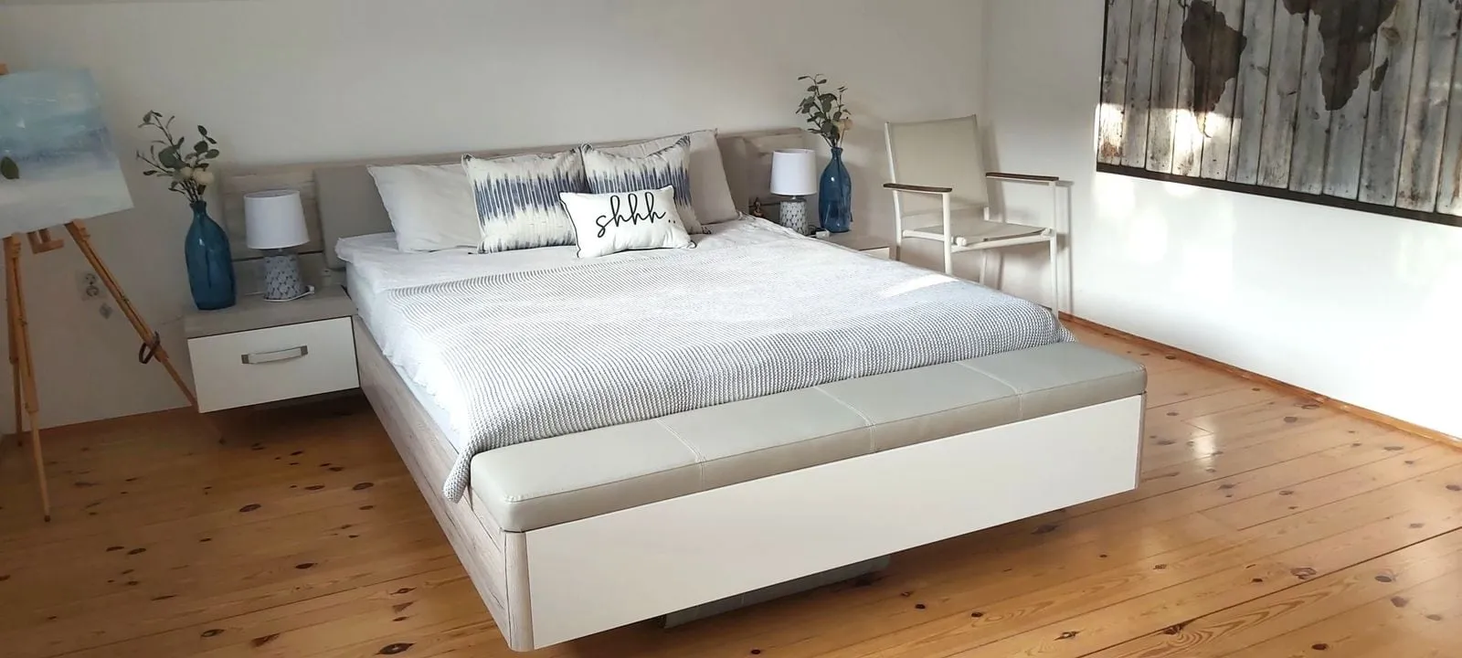 Modern bedroom featuring a large bed with white nightstands, blue vases, and wooden flooring.