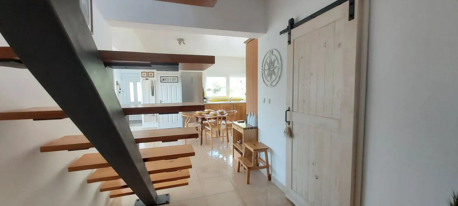 Floating wooden stairs leading to an open kitchen and dining area with a sliding barn door.