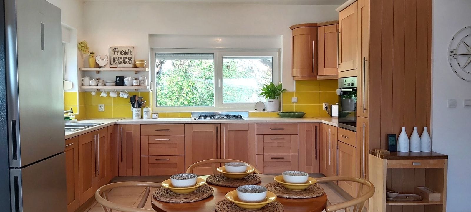 Cozy kitchen with wooden cabinets and a yellow backsplash in a house, Krymovitsa, Montenegro. Dining area and garden view.