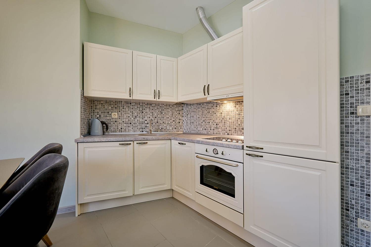 Bright corner kitchen with white cabinetry and a mosaic backsplash in an apartment for sale in Becici, Montenegro.