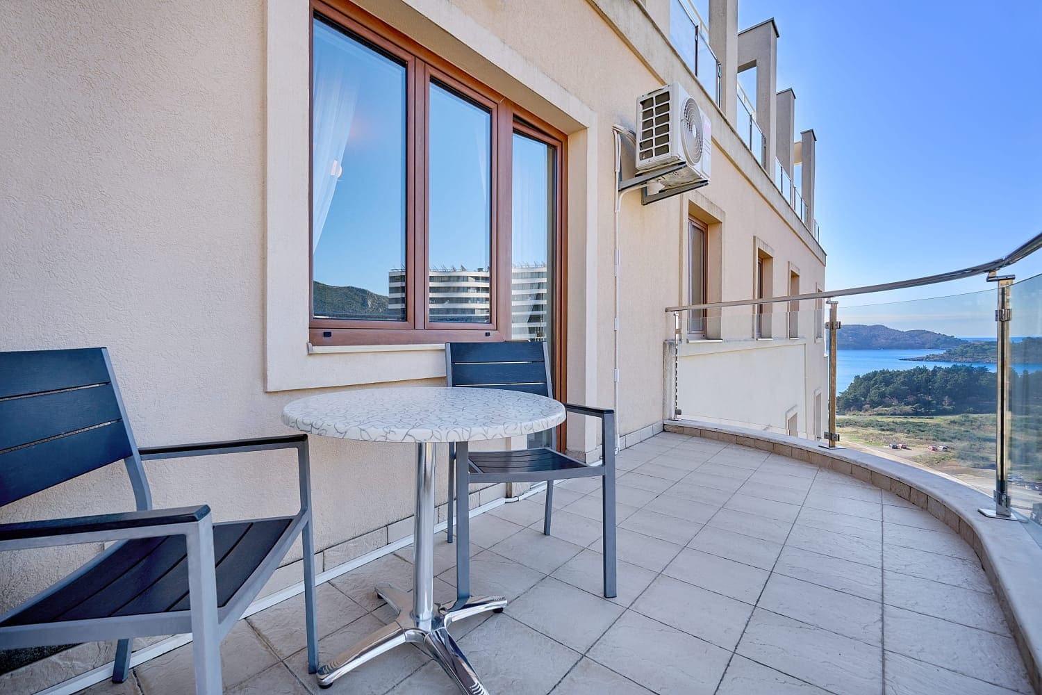 Apartment balcony in Becici, Montenegro: table with chairs, panoramic sea and mountain views, modern finishes.