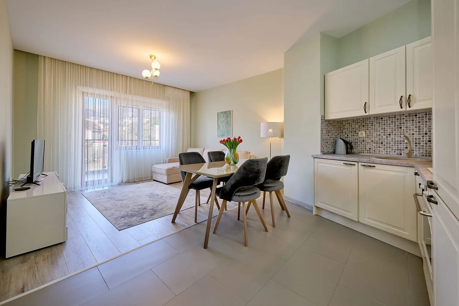Open plan space combining kitchen, dining table with chairs, and living area sofa.
