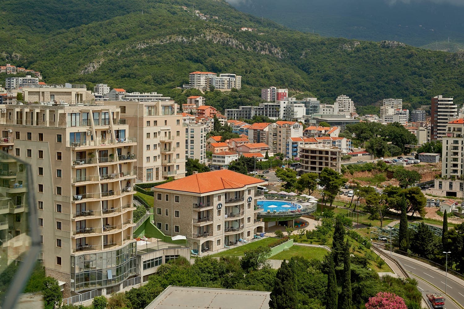 Panoramic view of a residential complex with a swimming pool and mountains in Bečići, Montenegro: modern houses and urban infrastructure.