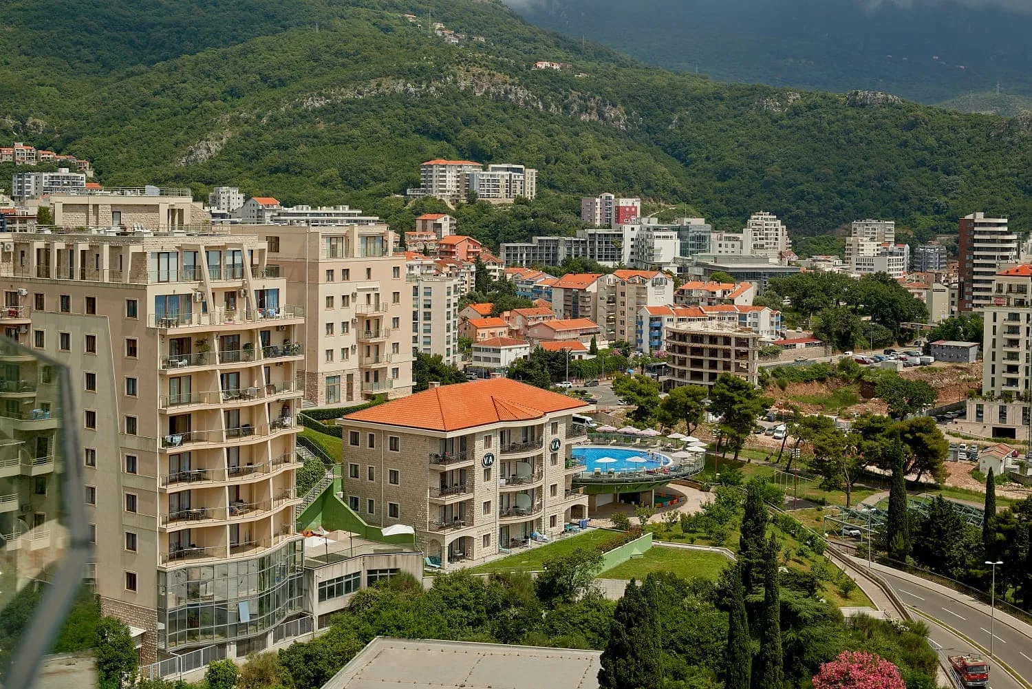 Panoramic view of city buildings, mountains, and an outdoor pool.