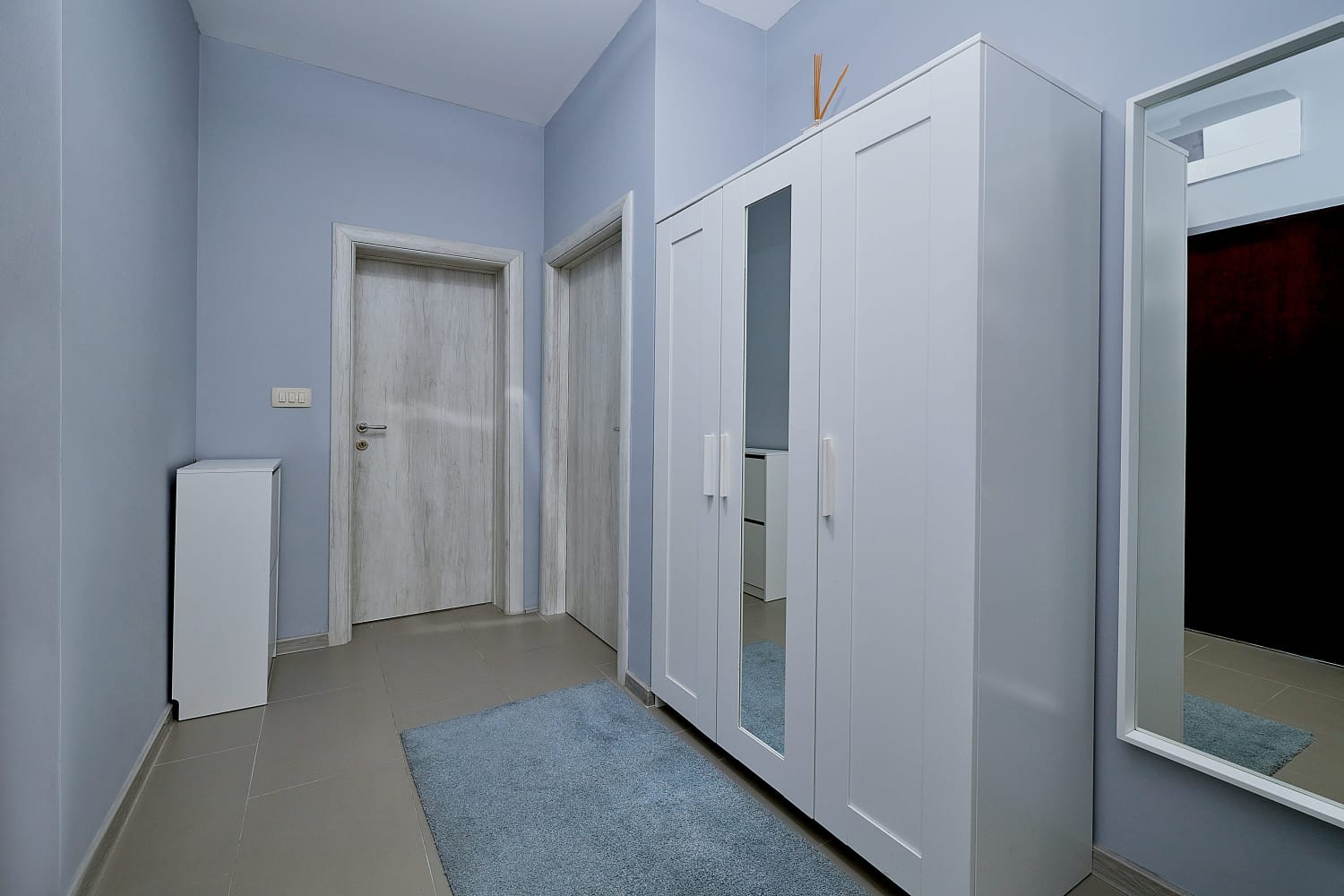 Bright hallway in an apartment in Bečići, Montenegro: white wardrobe with a mirror, gray doors, and tiled flooring in the interior.
