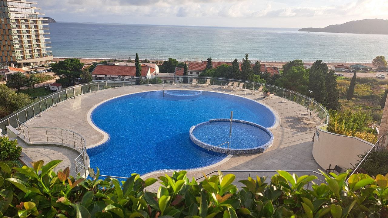 Outdoor swimming pool with a sea view in a residential complex in Bečići, Montenegro: terrace with sun loungers and panoramic views.