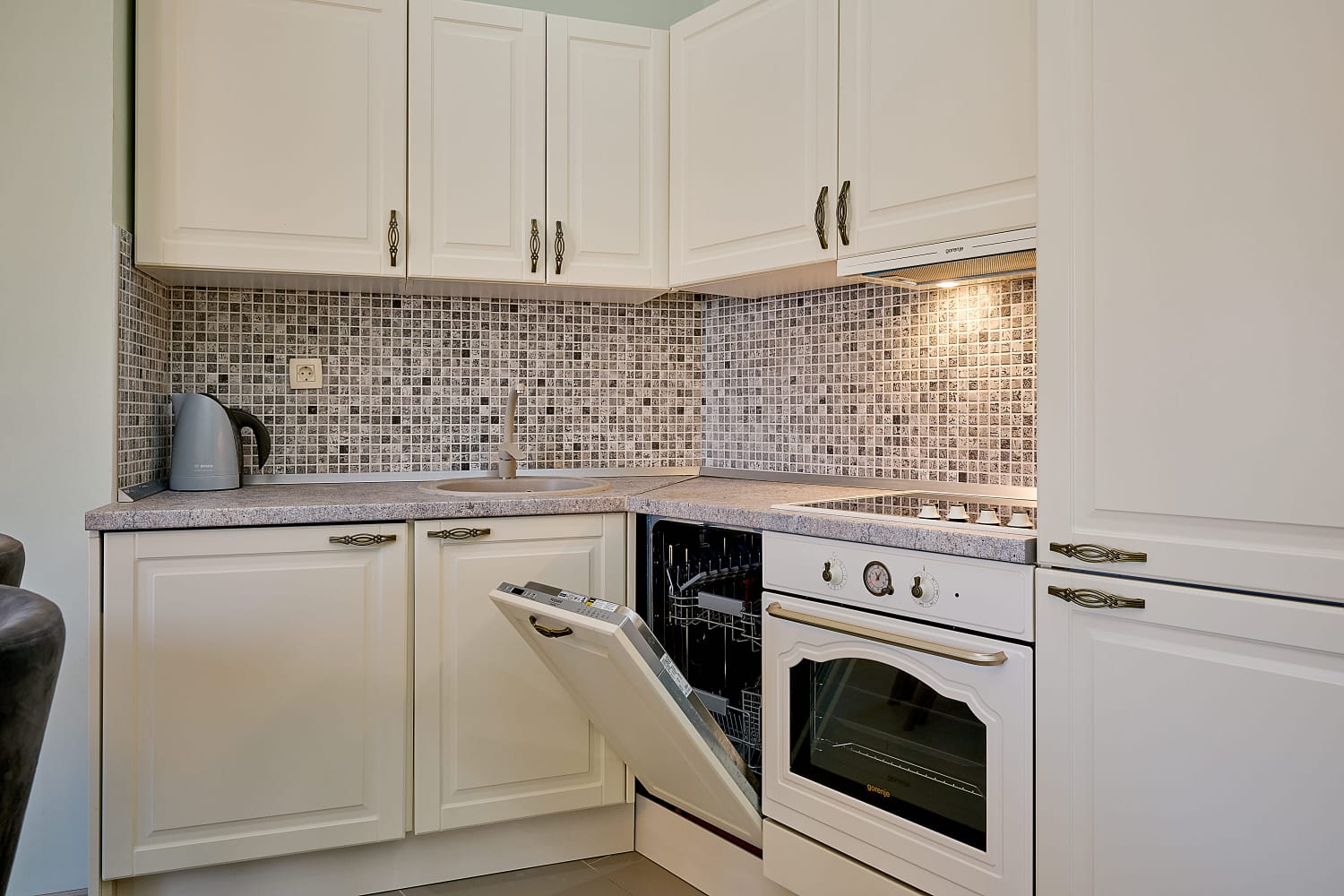 Bright kitchen in an apartment in Bečići, Montenegro: white cabinetry, built-in Gorenje appliances, and a mosaic backsplash.