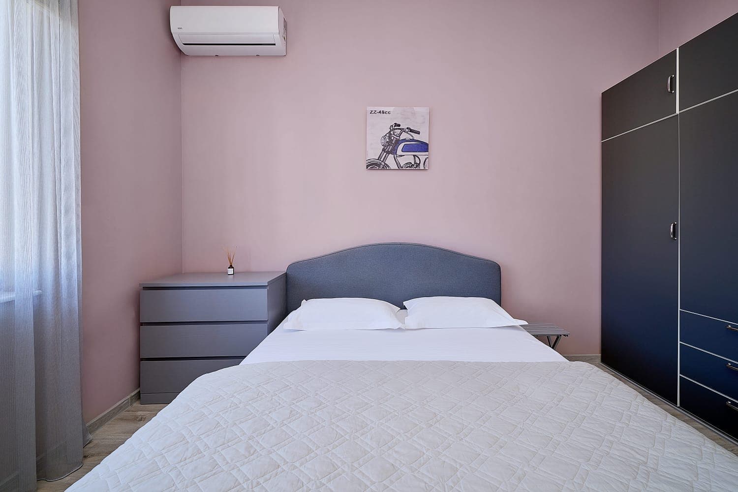 Bedroom in an apartment in Bečići, Montenegro: double bed, grey chest of drawers, wardrobe, and air conditioning in a modern interior.