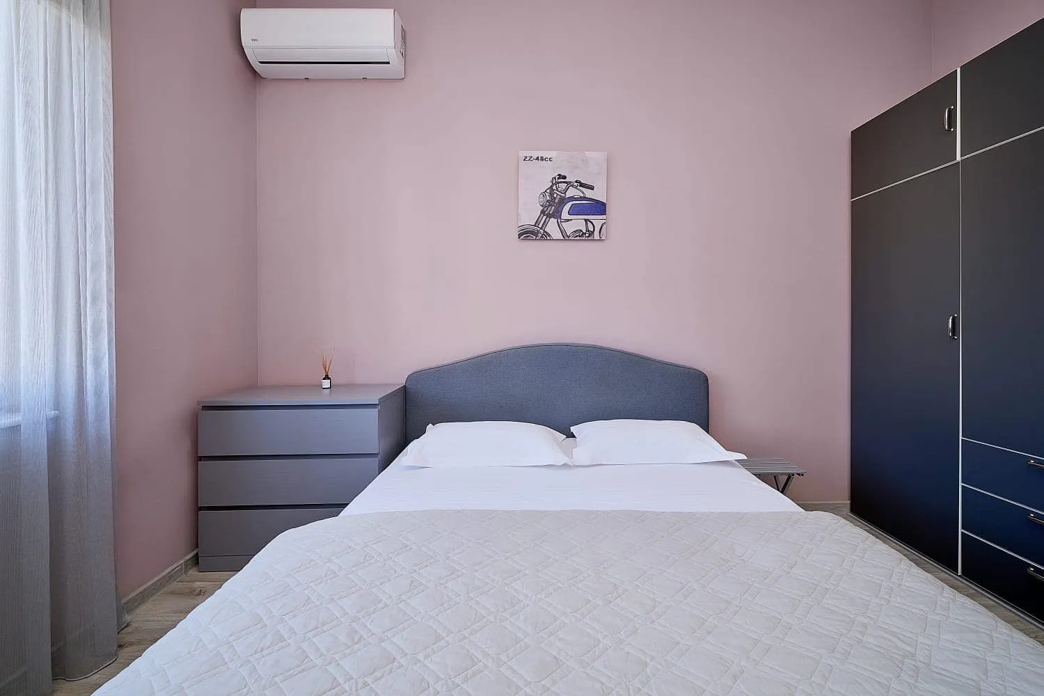 Bedroom with pink walls, a bed featuring a grey headboard, a nightstand, and a dark wardrobe.