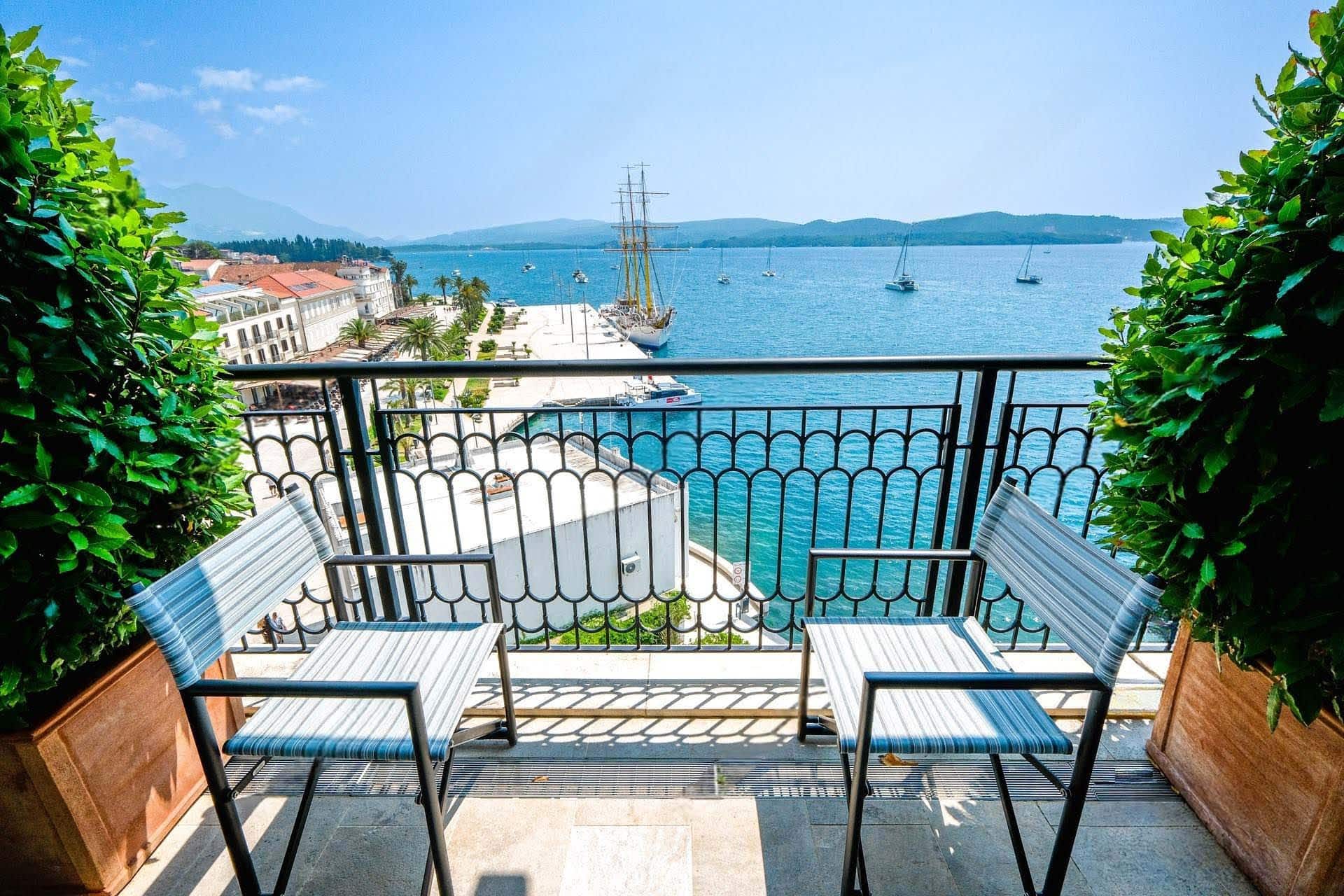 Balcony with a view of the marina and yachts in Tivat, Montenegro: two chairs, wrought-iron railing, and decorative plants.