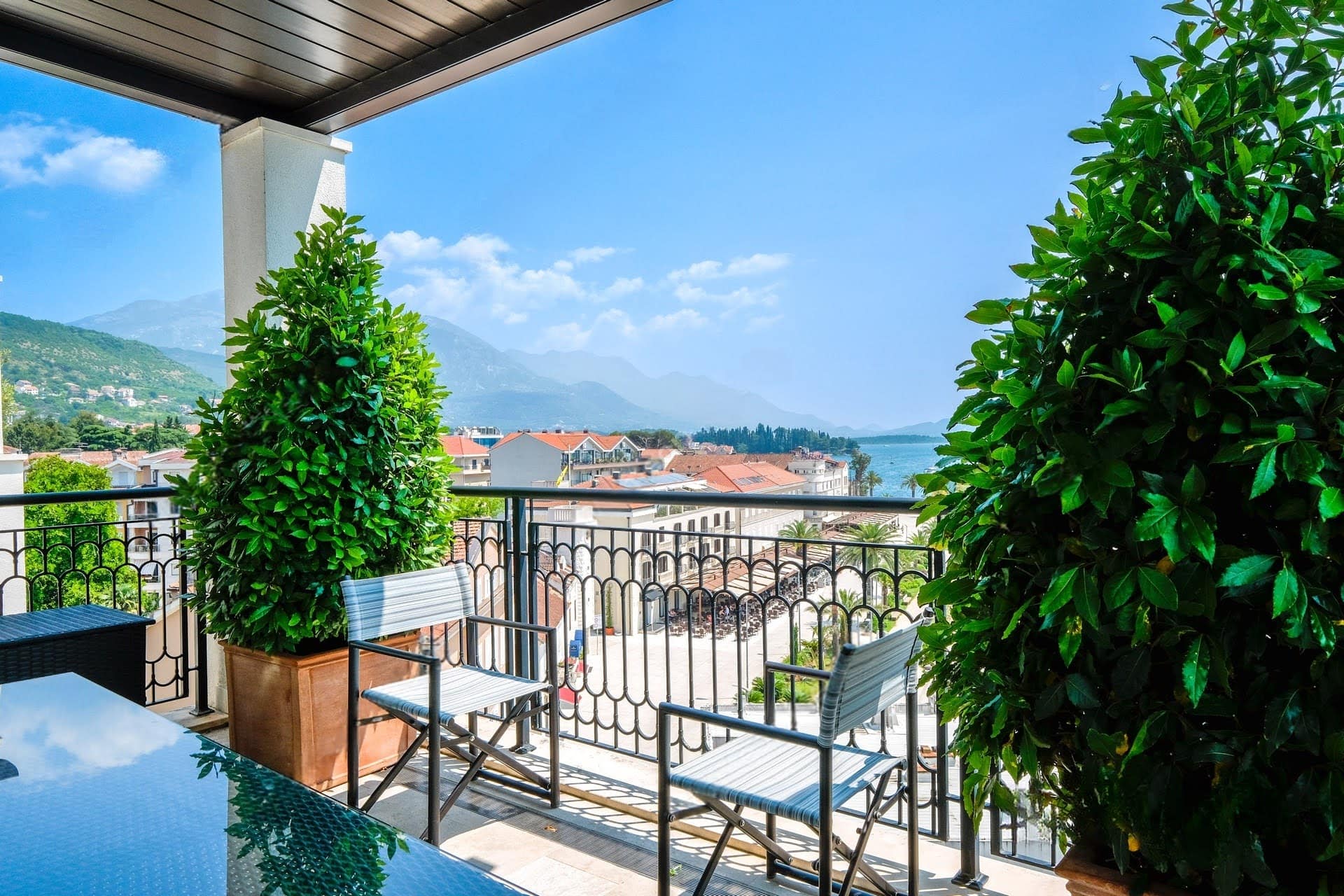Apartment terrace in Tivat, Montenegro: sea and mountain views, wrought-iron railings, garden furniture, and decorative plants.