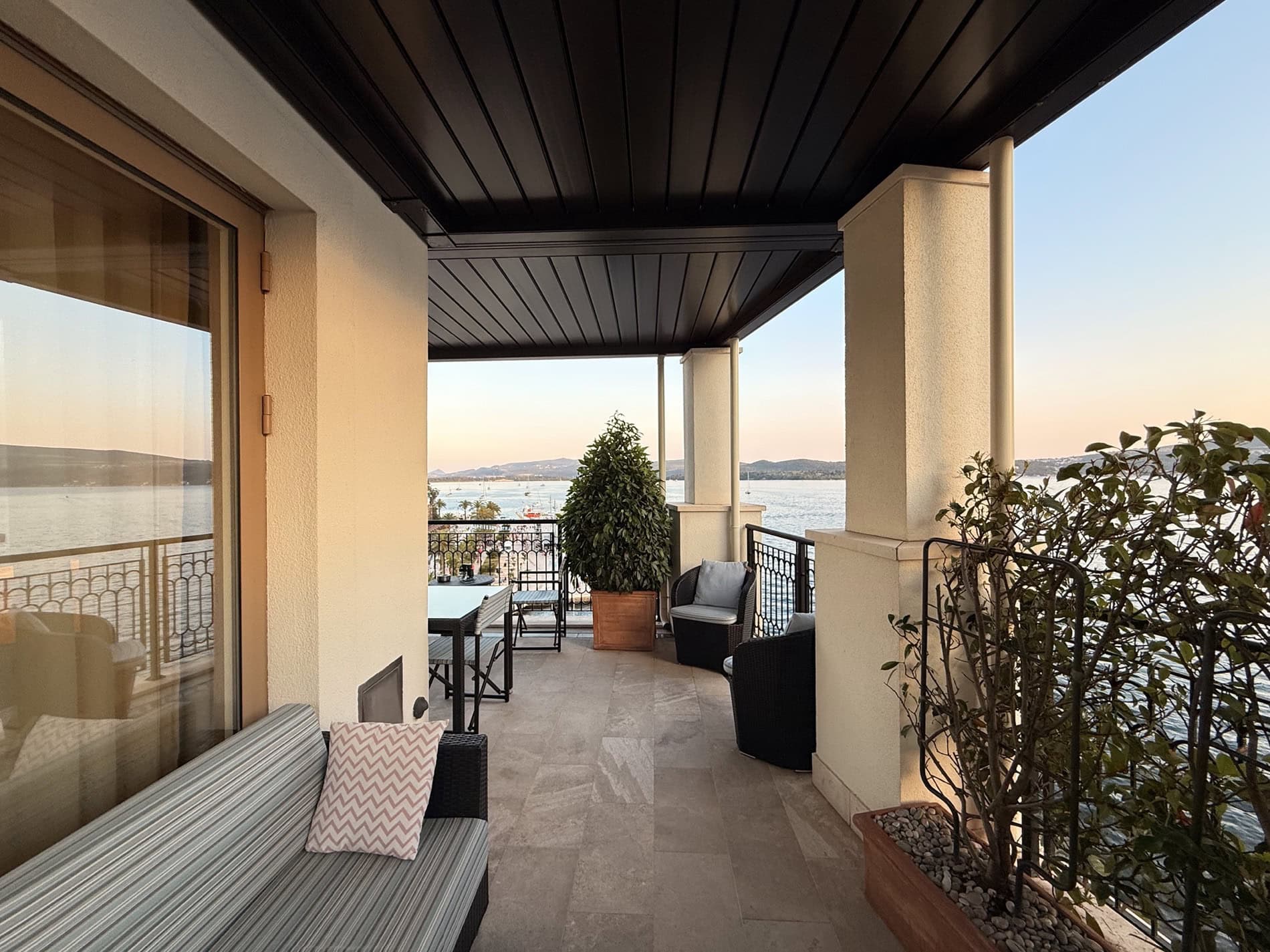 Terrace with furniture and sea view in an apartment in Tivat, Montenegro: a cozy seating area with wicker chairs and plants.