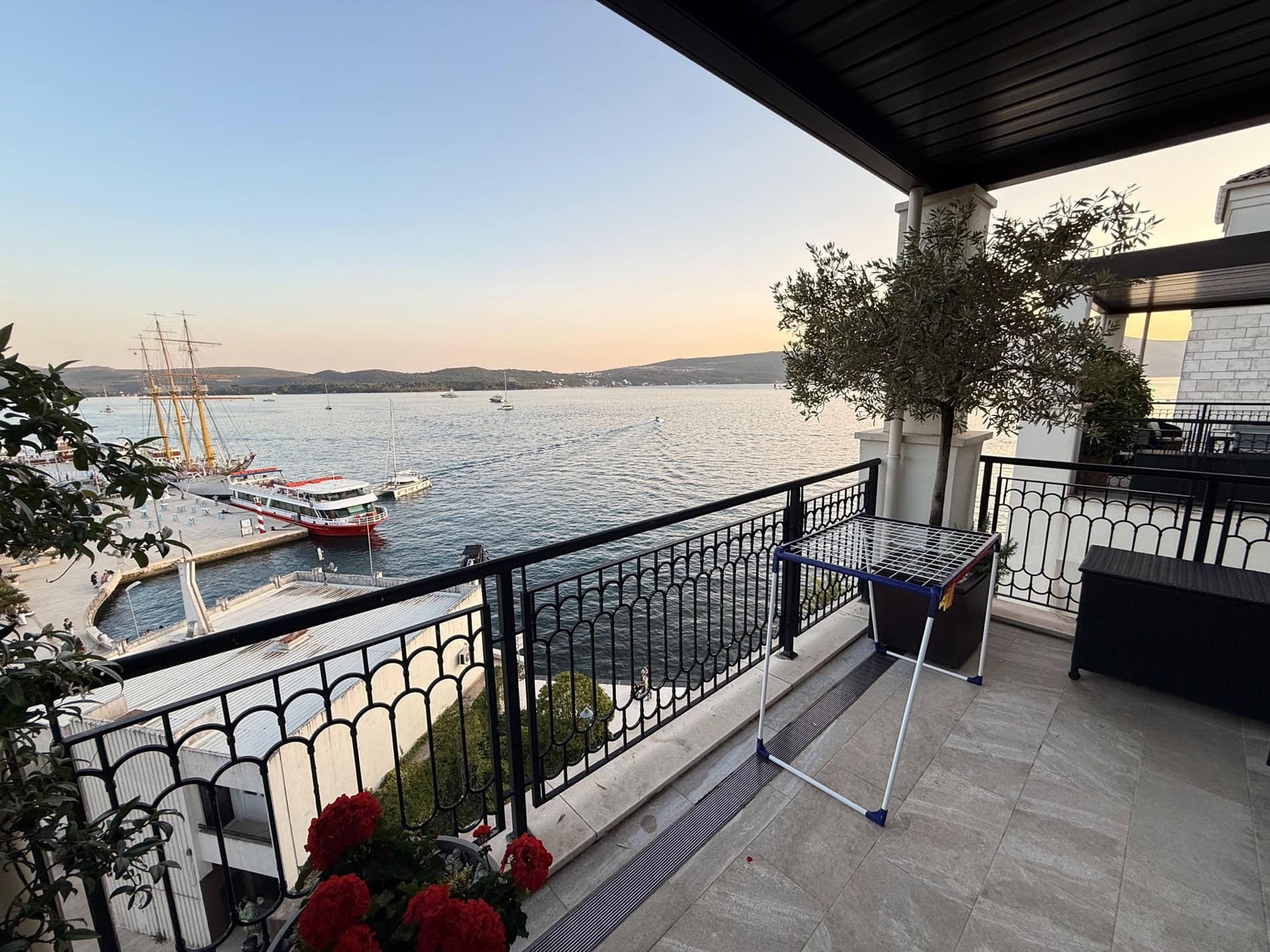 View from the apartment terrace in Tivat, Montenegro: panoramic sea, yachts and mountains, tiled flooring and wrought-iron railings.