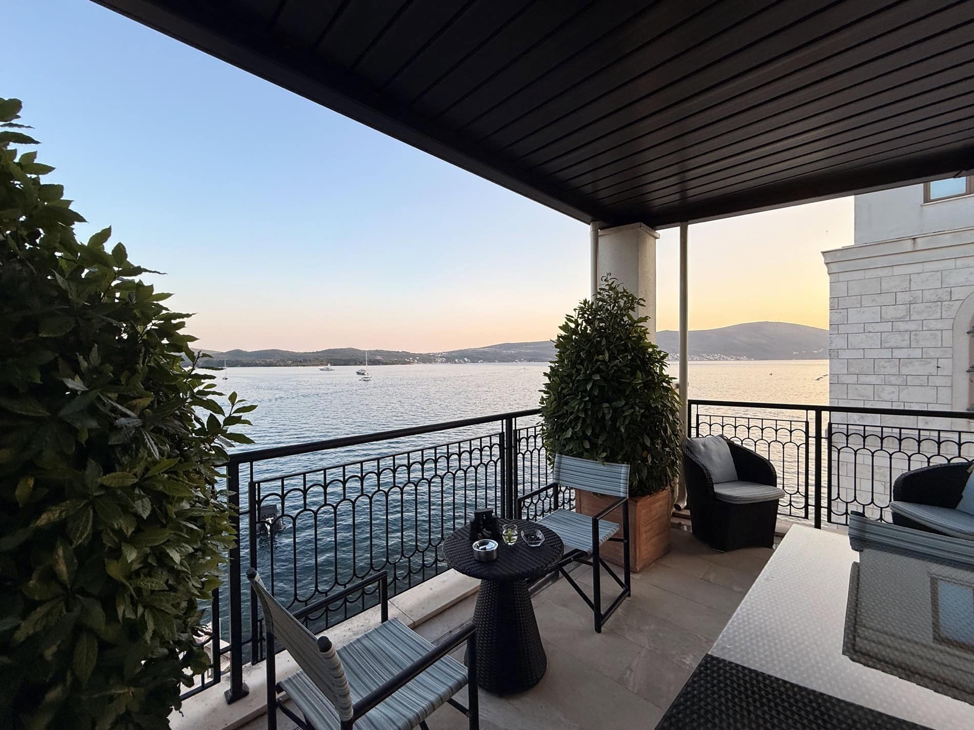 Terrace with wicker furniture and sea view in an apartment in Tivat, Montenegro. Cozy balcony with an awning and plants.