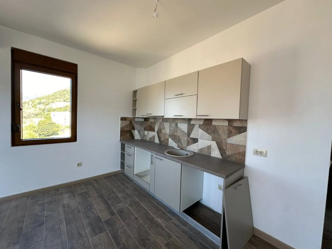Kitchen with beige upper cabinets, grey countertop, sink, geometric backsplash, and wood-look flooring.