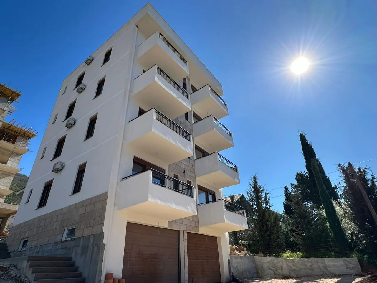 Exterior view of a multi-story residential building with balconies and garage doors under a sunny sky.