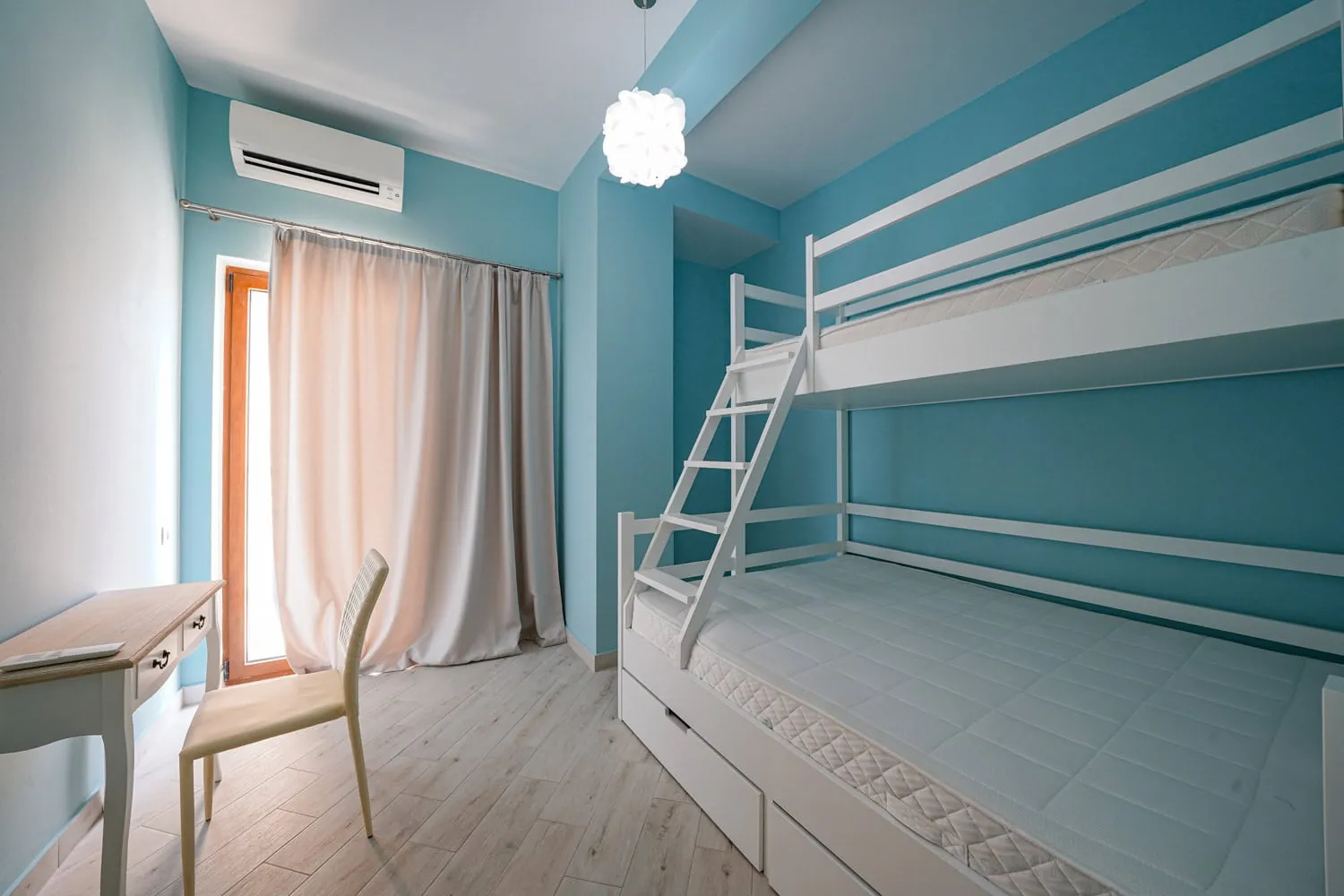 Bright bedroom featuring a white bunk bed, desk, chair, and light blue walls.