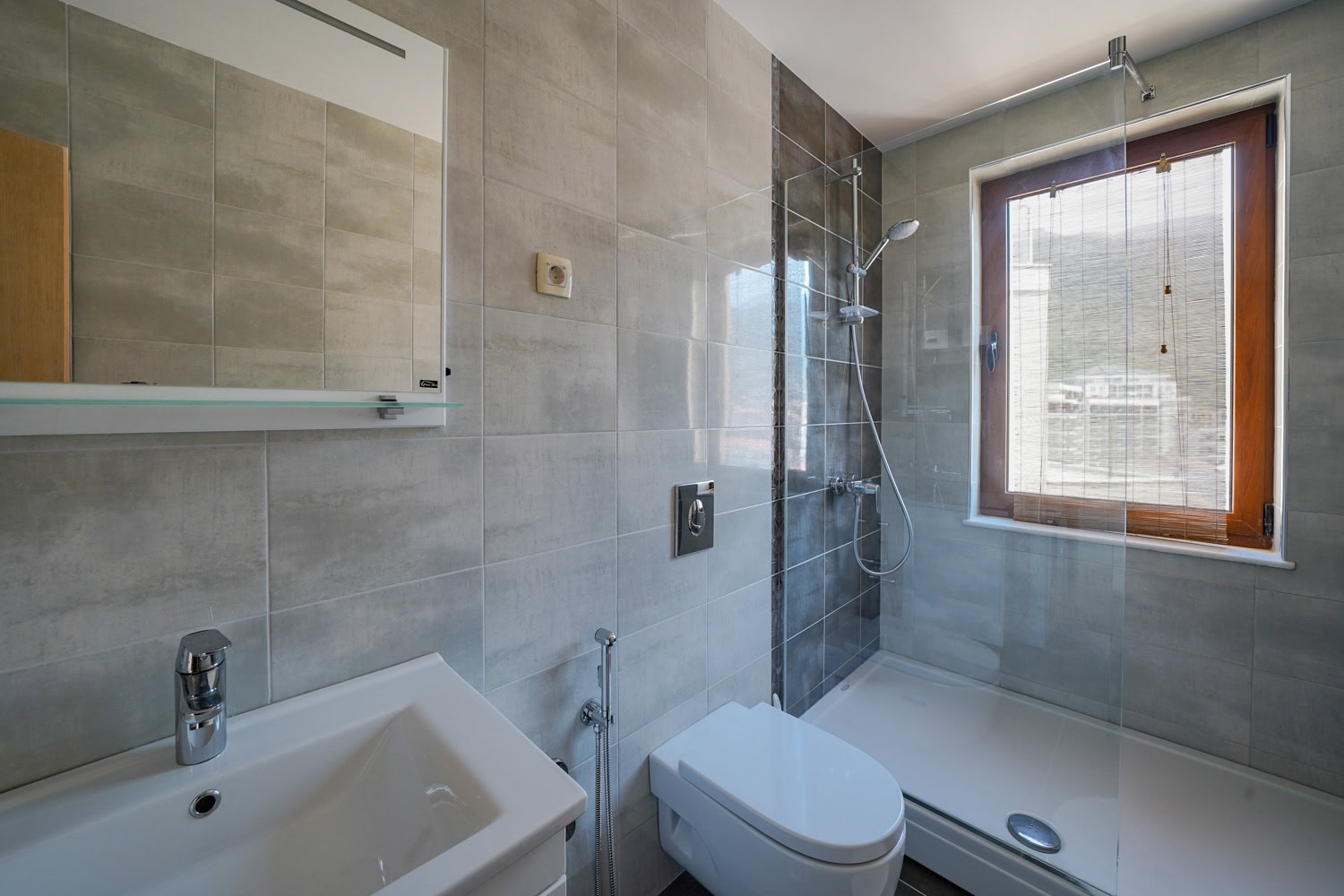 Modern bathroom in an apartment, Bečići, Montenegro: walk-in shower, wall-hung toilet, and a window with a view.