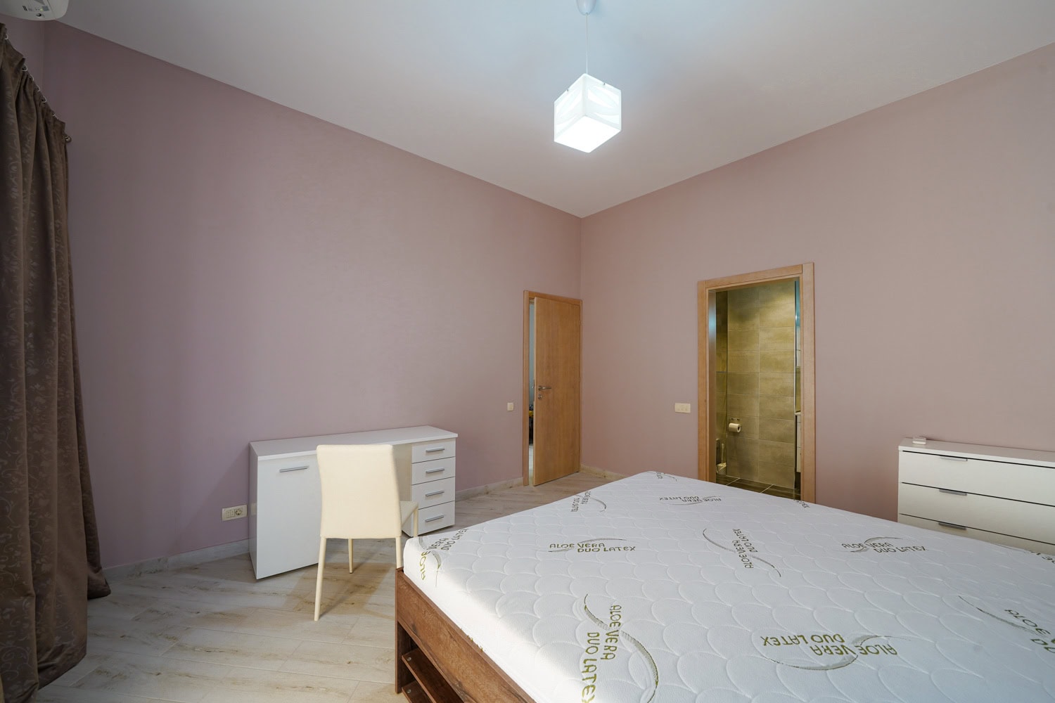 Bedroom in an apartment in Bečići, Montenegro: double bed, white desk, dresser, and entrance to the bathroom.