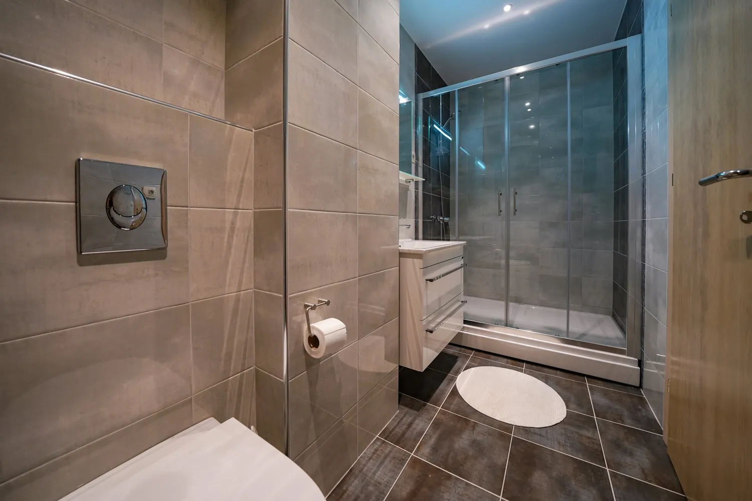 Modern bathroom featuring a glass shower enclosure, toilet, vanity unit, and grey wall tiles.