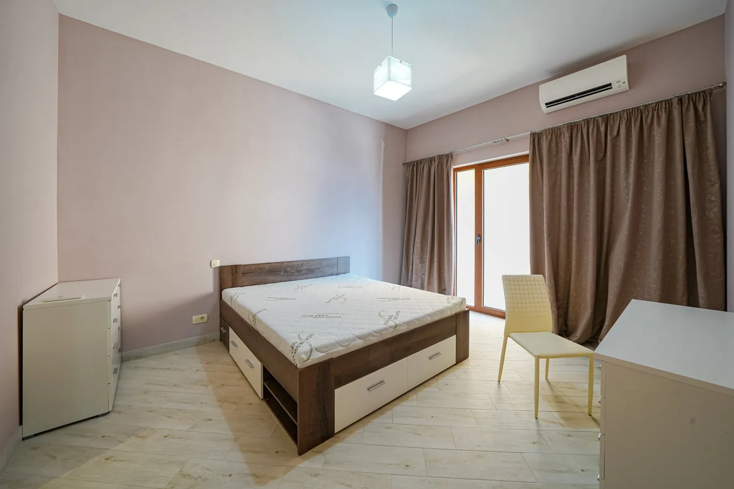 Bedroom featuring a wooden bed with storage, white dresser, yellow chair, and AC unit on pink walls.