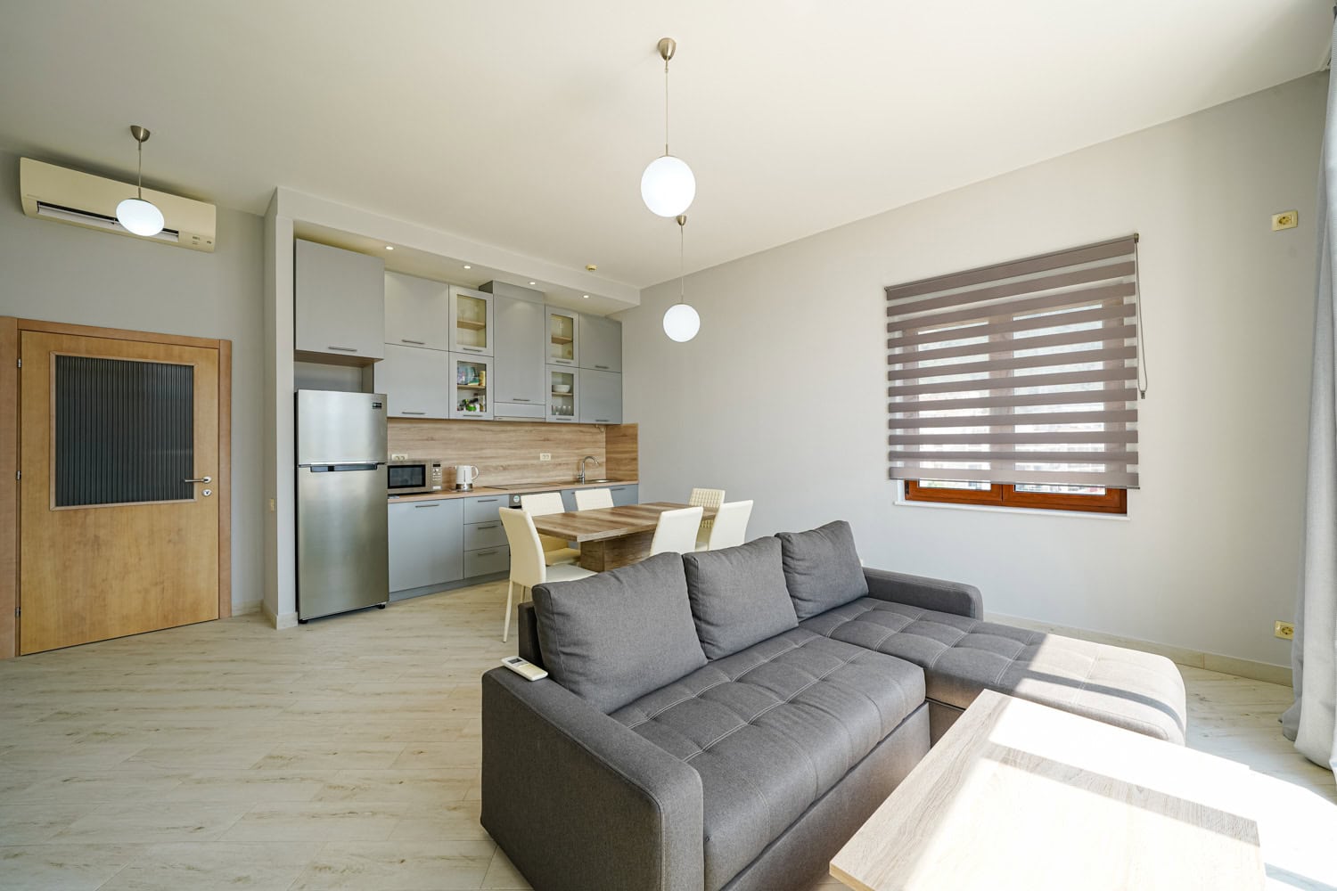 Modern living room with a kitchen in an apartment in Bečići, Montenegro: gray sofa, dining area, and bright interior.