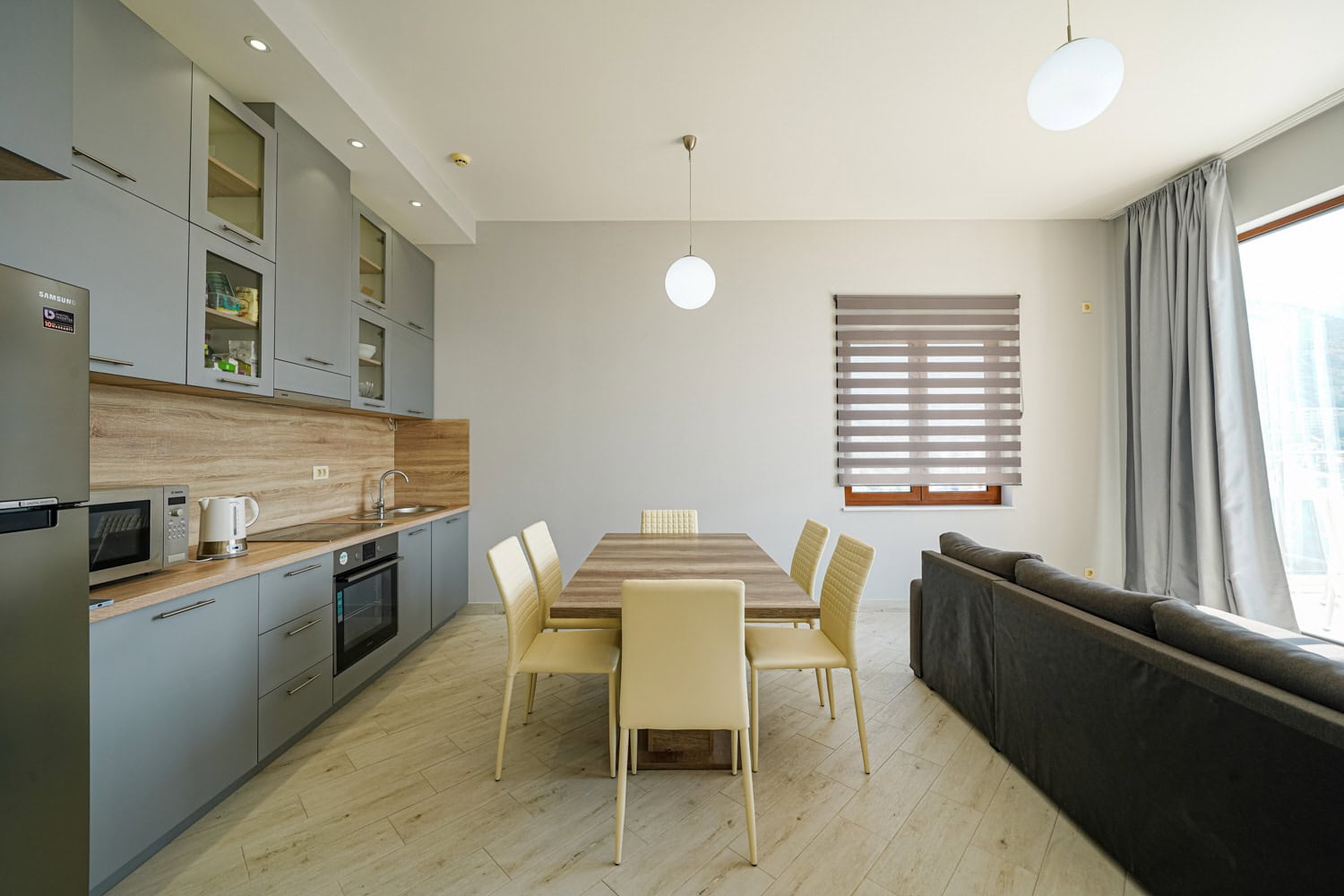 Modern kitchen-living room with a dining area in an apartment in Becici, Montenegro: grey kitchen cabinetry and light-colored furniture.