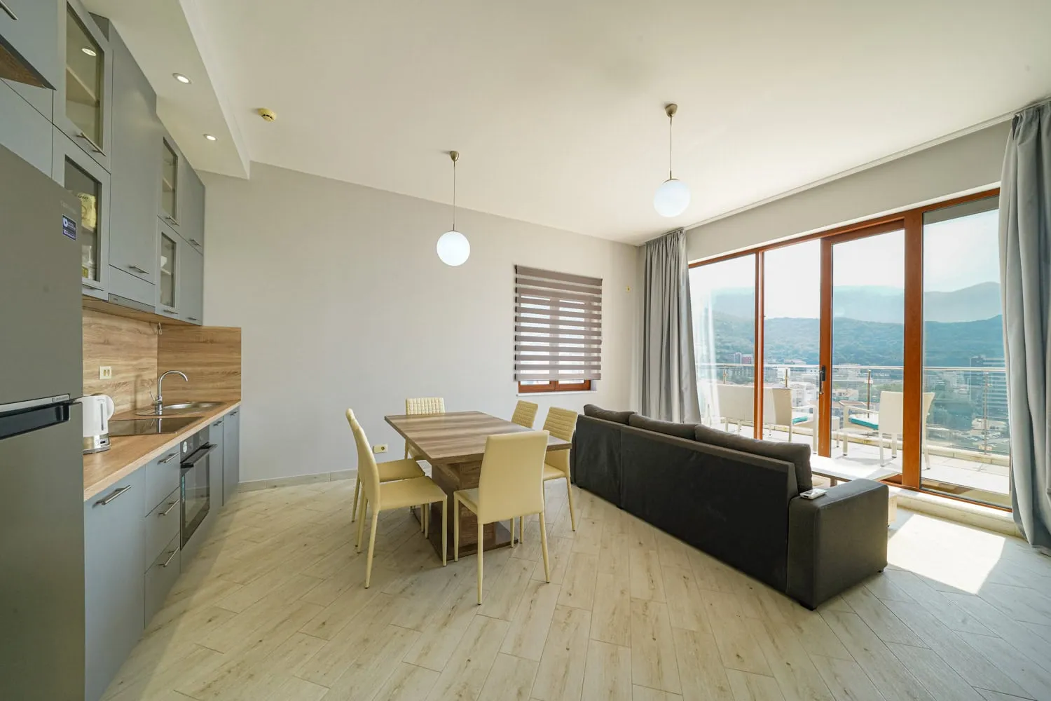 Open plan living room with kitchenette, dining table, sofa, and large windows.