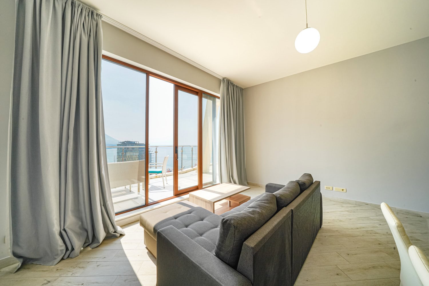 Living room with floor-to-ceiling windows and sea views in an apartment, Becici, Montenegro: modern sofa and access to the terrace.