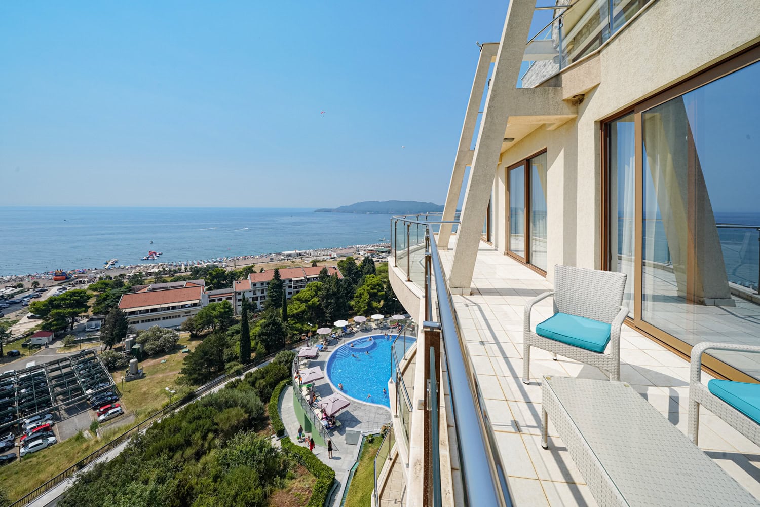 Spacious balcony with furniture and panoramic views of the sea, beach, and swimming pool in Bečići, Montenegro.