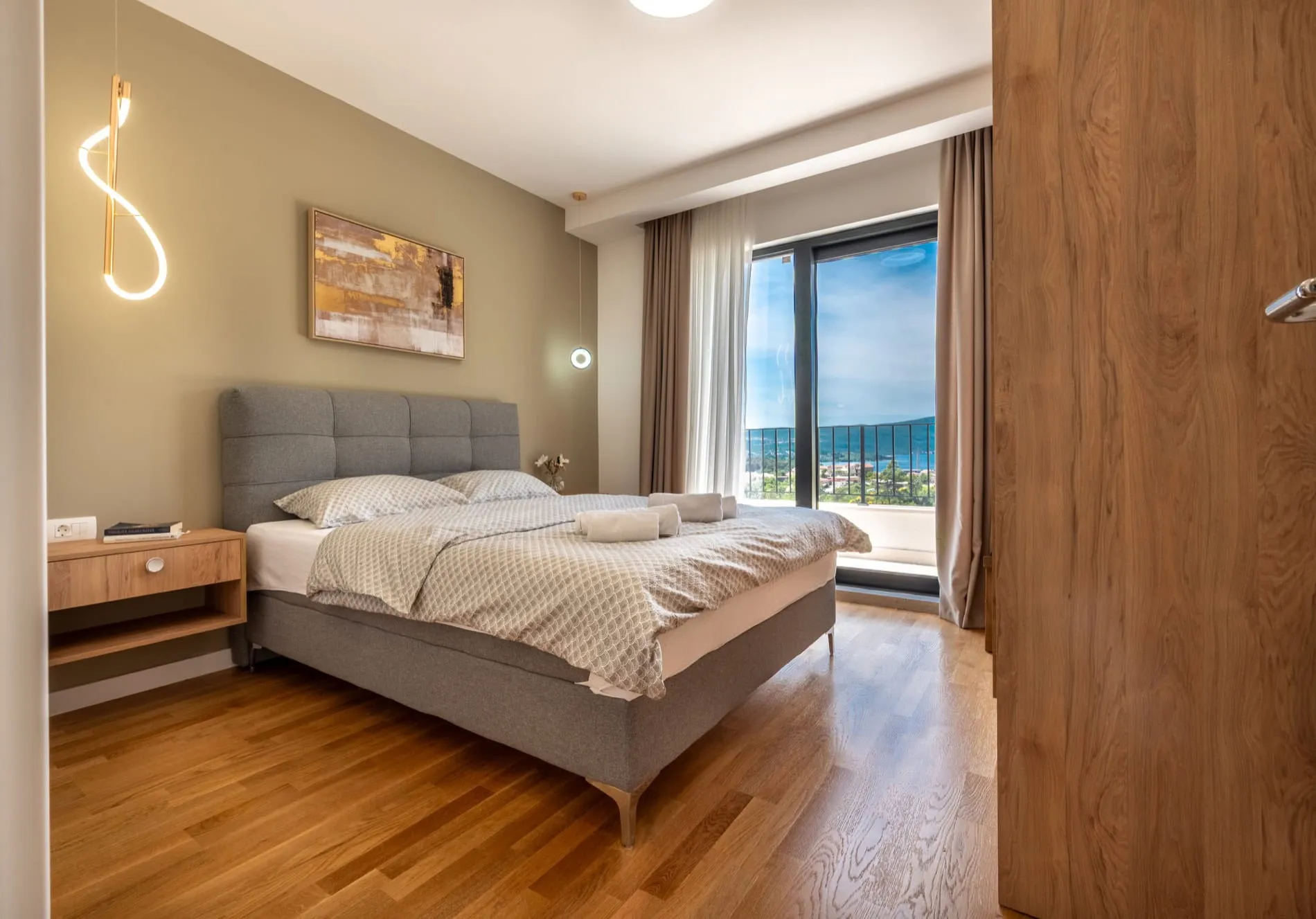 Modern bedroom featuring a grey upholstered bed, wooden flooring, and abstract wall art.
