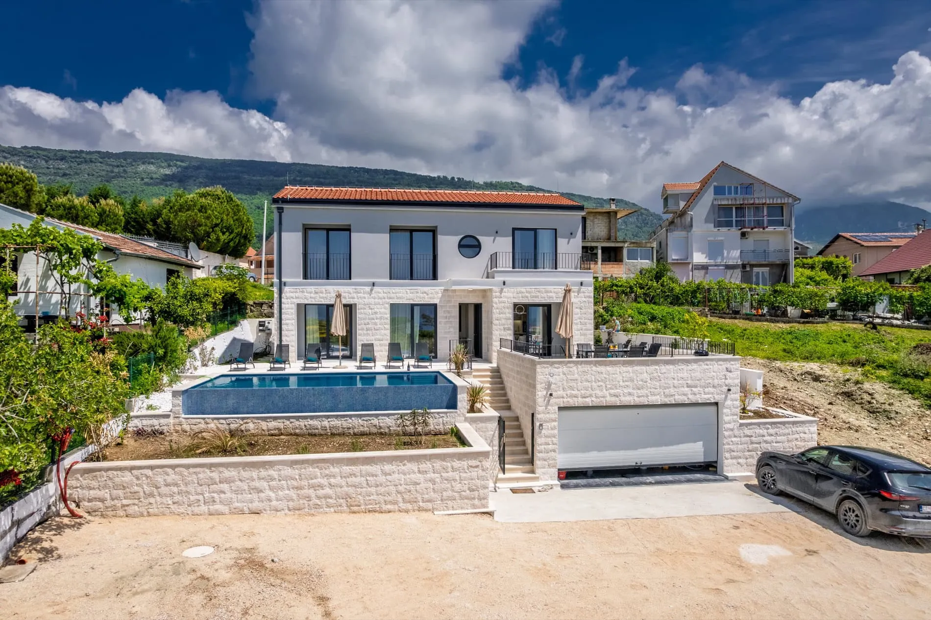 Exterior view of a two-story house with a pool, garage, and terrace against mountains.