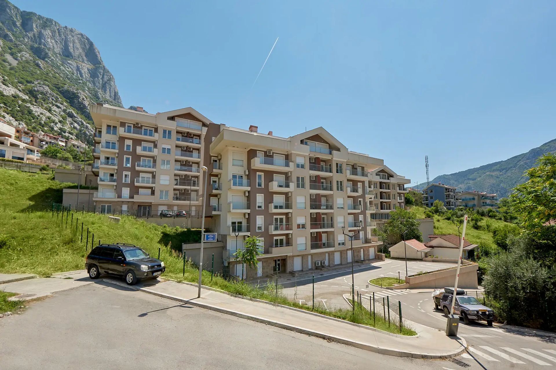 Modern residential complex in Dobrota, Montenegro: view of an apartment building with parking and mountain landscape.