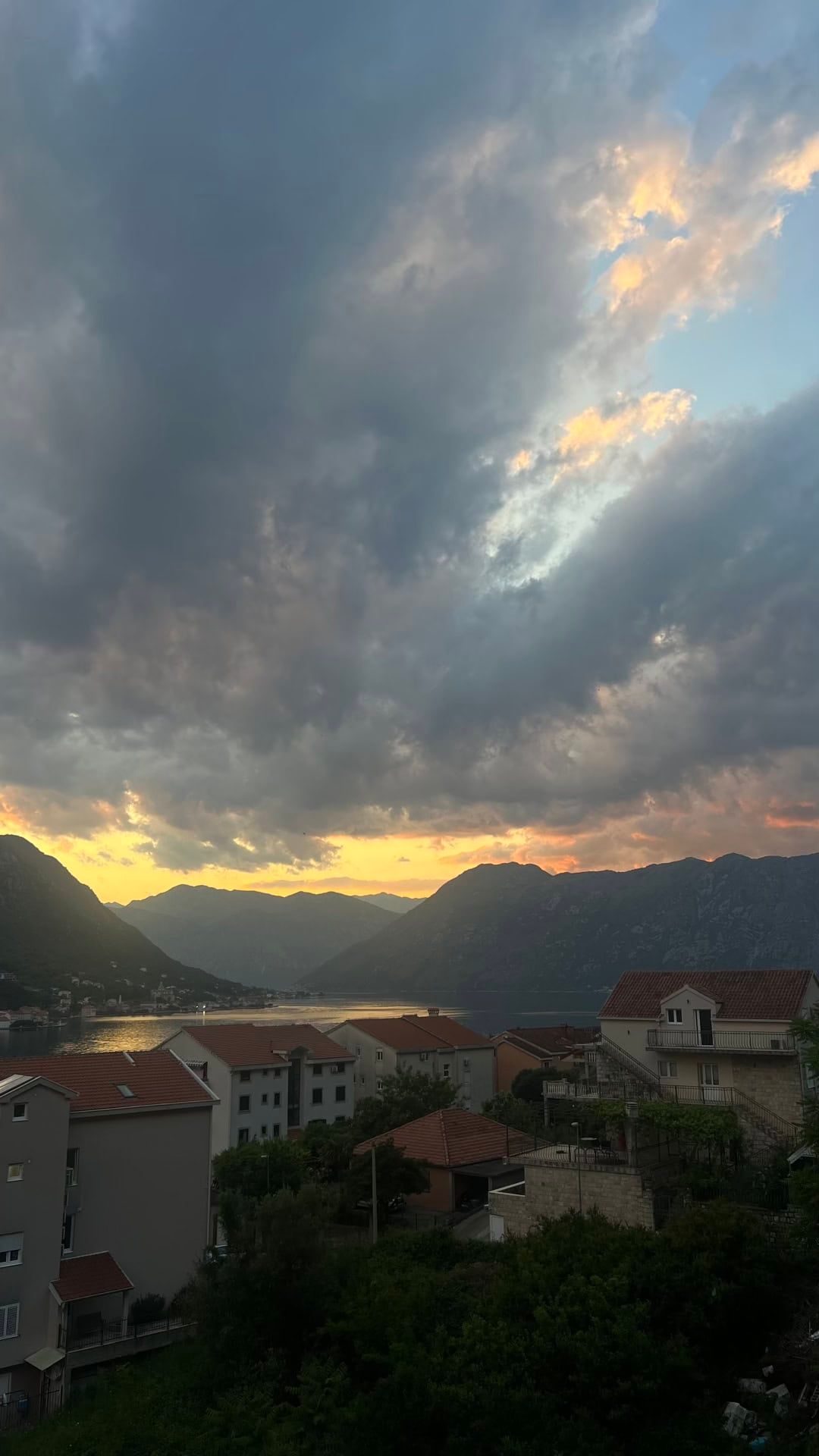 Panoramic view of the Bay of Kotor and mountains at sunset from an apartment in Dobrota, Montenegro, overlooking a residential area.