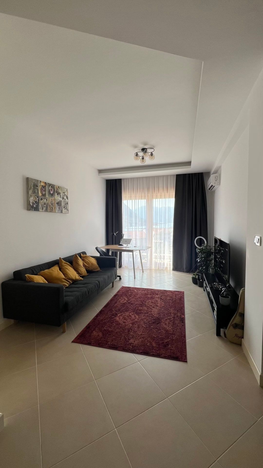Living room in an apartment in Dobrota, Montenegro: a black sofa with yellow cushions, a desk, and a mountain view from the window.