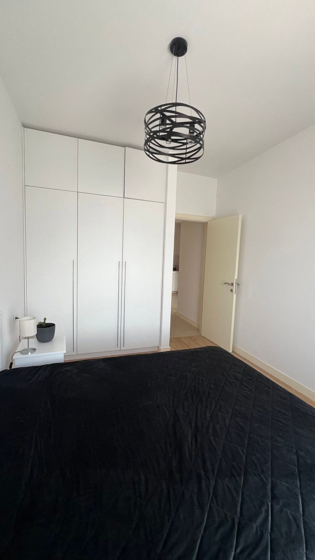 Bedroom in an apartment in Dobrota, Montenegro: white wardrobes, a black bedspread, and a modern chandelier in the interior.