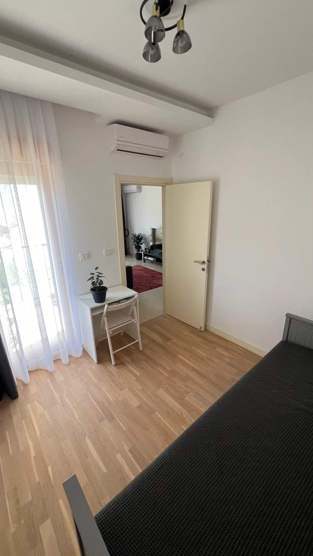 Bedroom featuring a bed, white desk, chair, air conditioner, and light wood flooring.