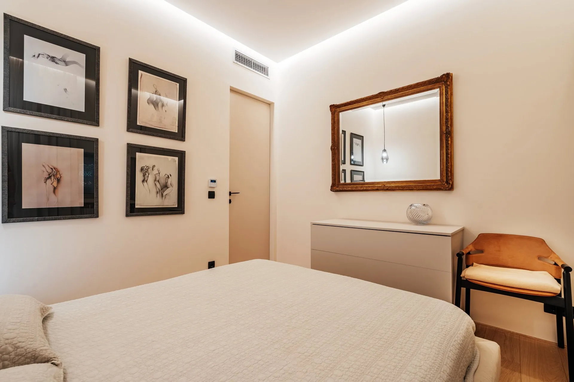 Modern bedroom featuring a large bed, white dresser, ornate gold mirror, and four framed art prints on the wall.