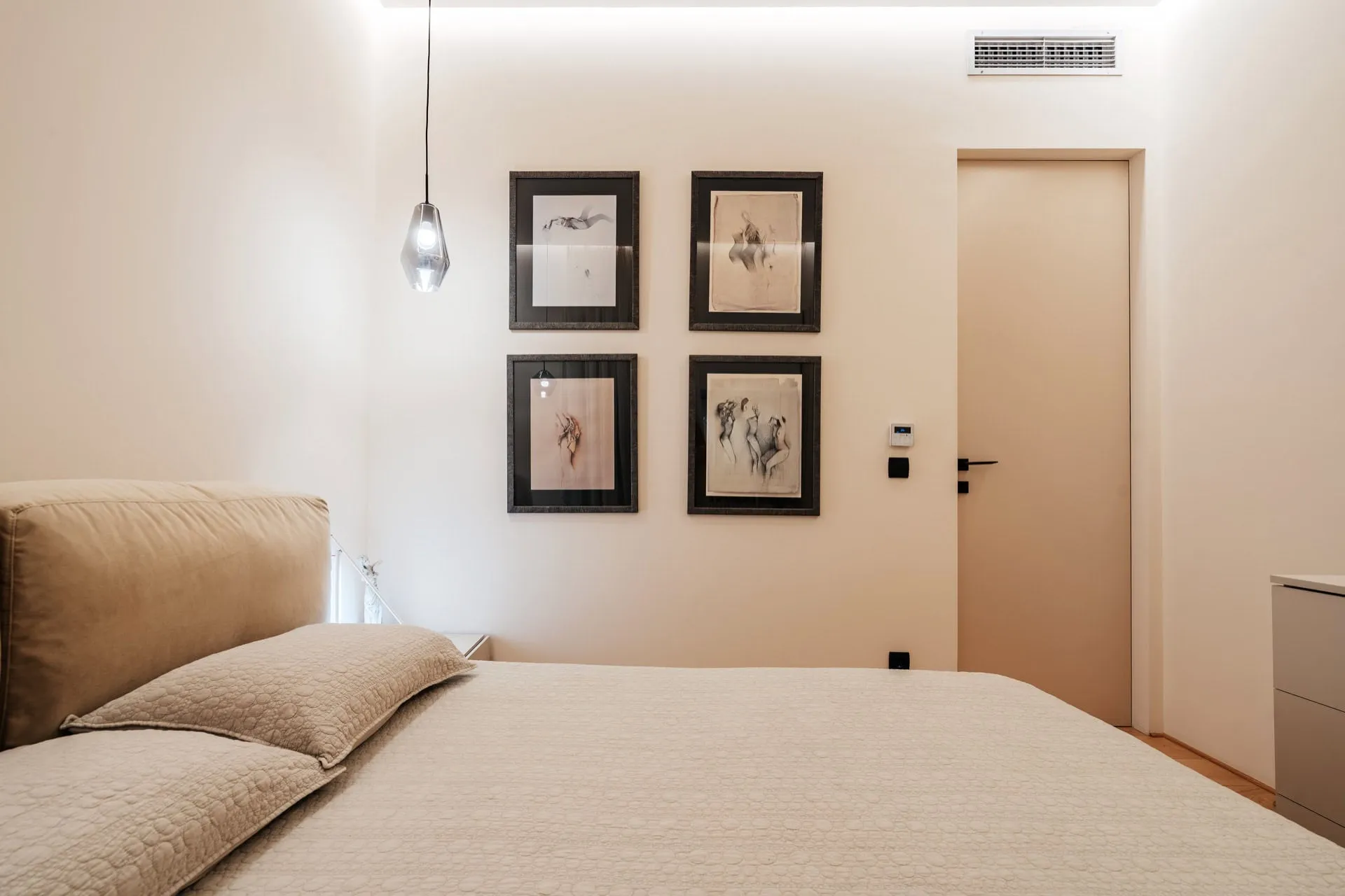 Modern bedroom featuring a large bed, pendant light, and four framed art prints on the wall.