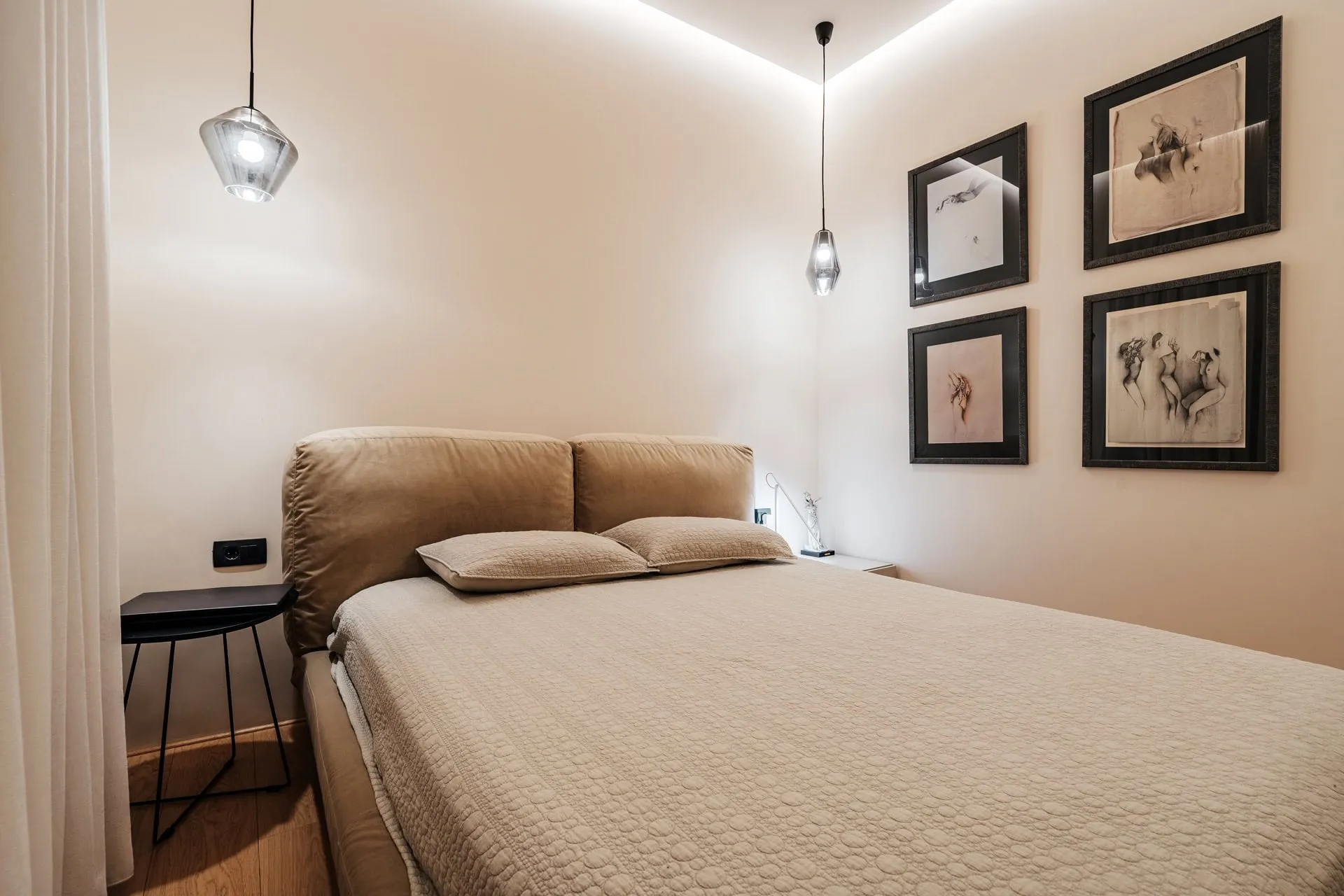 Modern bedroom featuring a large beige bed, glass pendant lights, and four framed art prints on the wall.