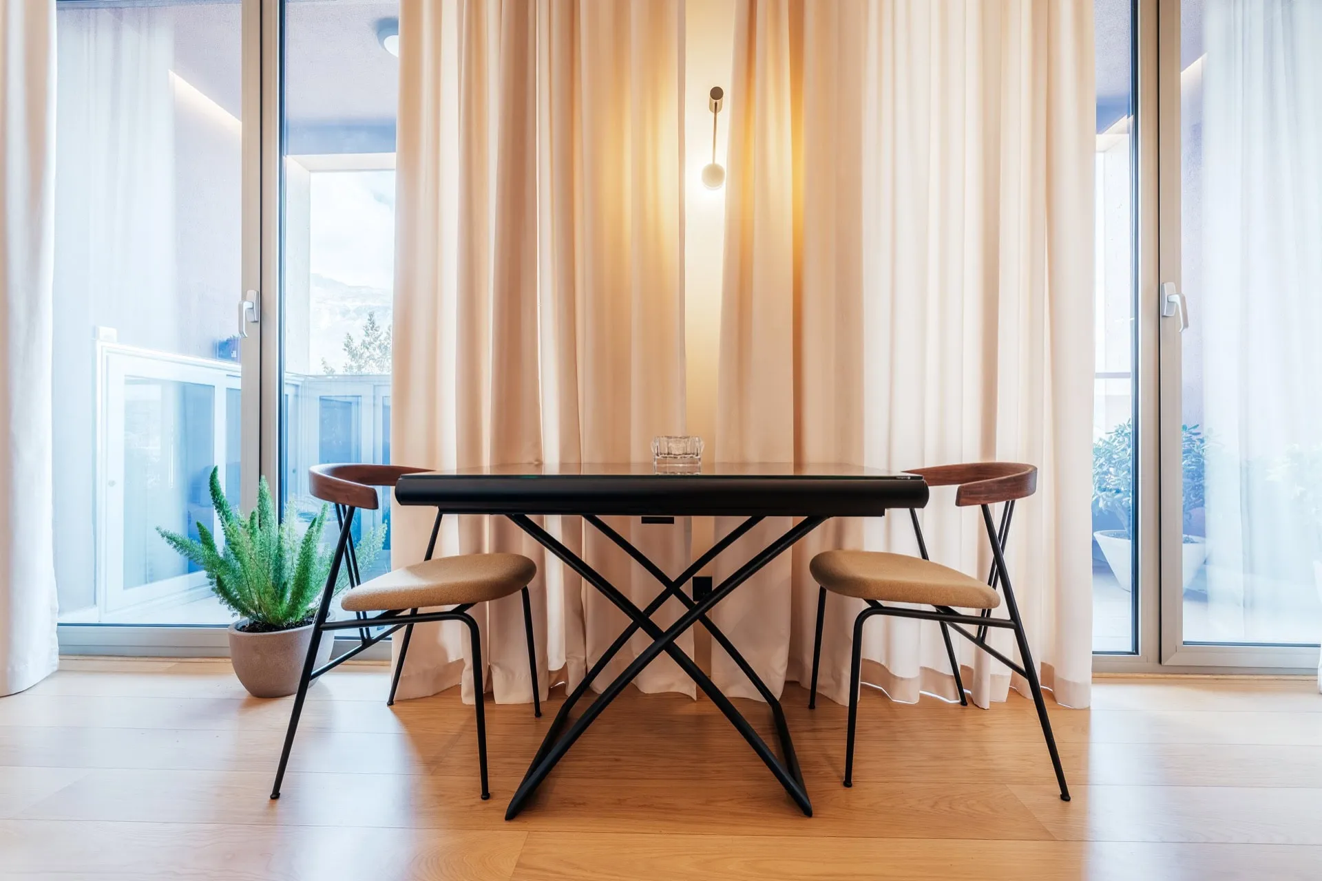 Bright room with a black table, two chairs, and a green plant near a window with beige curtains.