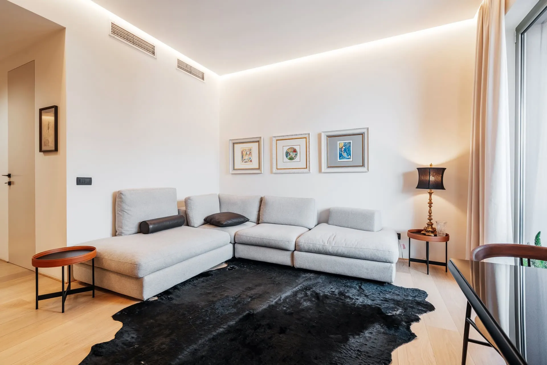 Bright room with a gray sectional sofa, black cowhide rug, framed art, and ambient ceiling lighting.