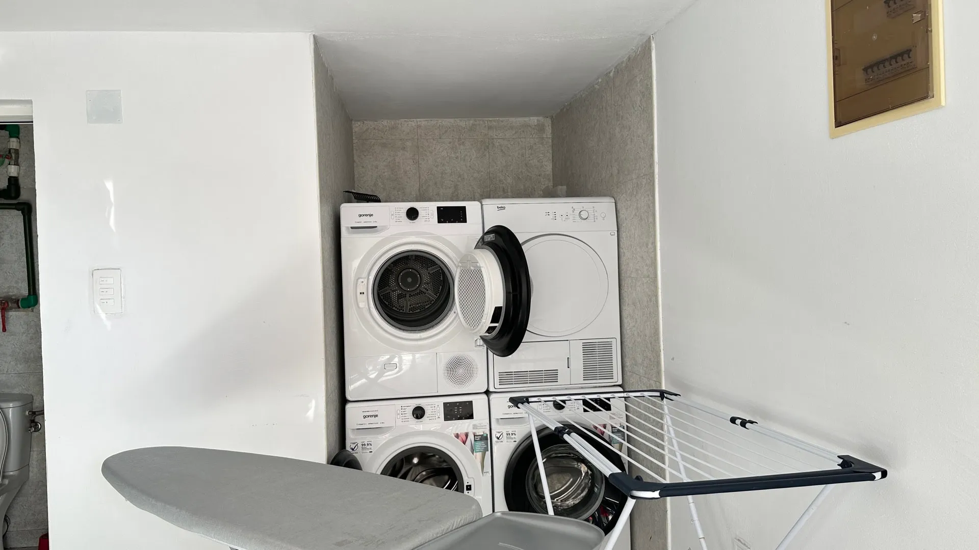 Washer and dryer units, ironing board, and drying rack visible in a utility or laundry area.