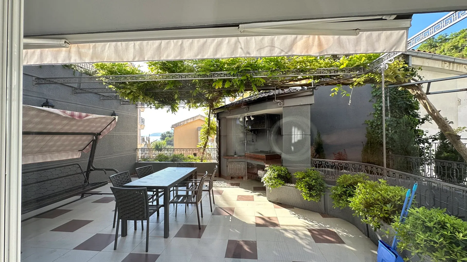 Open terrace with dining table, outdoor kitchen, and green pergola over tiled flooring.