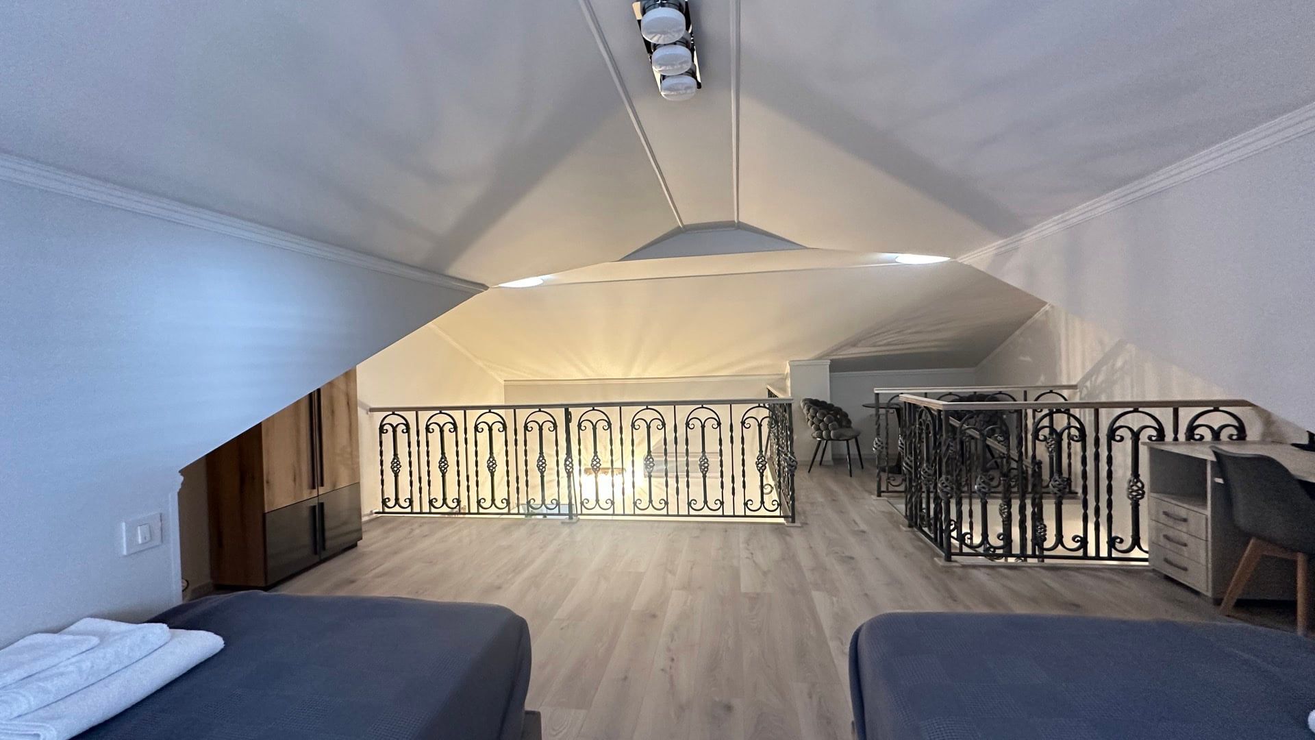 Attic bedroom in a hotel in Pržno, Montenegro: bright interior, wrought-iron railings, modern furniture, and a sloped roof.